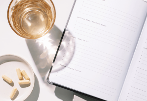 Ein Flatlay Foto von einem Planer, Pillen und einem Glas Tee.