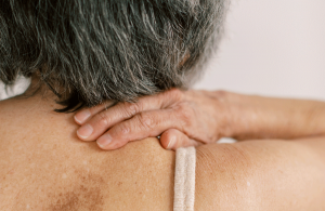 Dame mit grauen Haaren von hinten fasst sich an den Nacken um dort eine Verspannung zu symbolisieren.